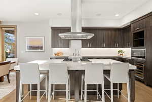 Kitchen featuring dark brown cabinets, modern cabinets, island range hood, a center island, and light wood finished floors