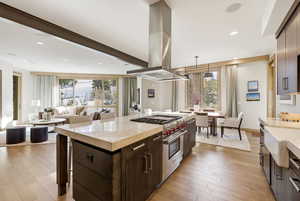 Kitchen with dark brown cabinetry, island exhaust hood, light stone counters, decorative light fixtures, and a center island