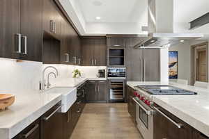 Kitchen with dark brown cabinets, island exhaust hood, luxury stove, light stone counters, and recessed lighting