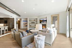 Living area with built in shelves, light wood-style flooring, a warm lit fireplace, and recessed lighting