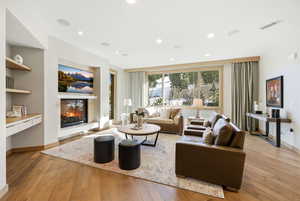 Living area with a glass covered fireplace, light wood-style flooring, recessed lighting, built in study area, and built in features