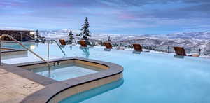 Snow covered pool featuring a patio, a hot tub, an outdoor pool, and a mountain view