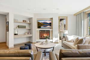 Living area featuring a warm lit fireplace, built in shelves, and light wood-type flooring
