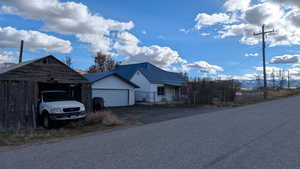 View of front facade with a garage, a metal roof, driveway, and an outbuilding. View looking South.
