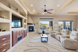 Living room with built in shelves, ceiling fan, a large fireplace, a raised ceiling, and recessed lighting