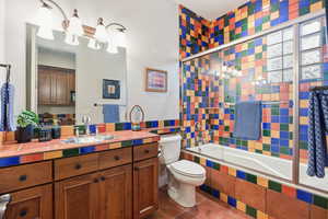 Bathroom with tiled shower / bath combo, vanity, dark tile patterned flooring, a chandelier, and tile walls