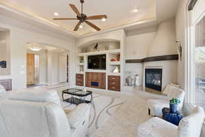 Living area with built in features, a fireplace, a ceiling fan, a raised ceiling, and recessed lighting