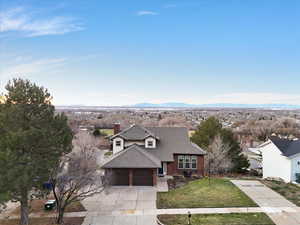 View of front of home with driveway, roof with shingles, a front yard, a chimney, and a mountain view
