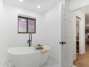 Bathroom with light marble finish flooring, a walk in closet, and a freestanding bath