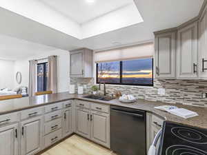 Kitchen with black appliances, backsplash, dark stone counters, light wood finished floors, and healthy amount of natural light