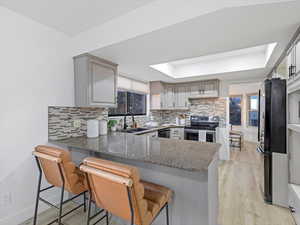 Kitchen with stainless steel appliances, a peninsula, a breakfast bar area, a tray ceiling, and light stone countertops