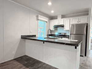 Kitchen with a peninsula, stainless steel appliances, white cabinets, dark wood-style floors, and ornamental molding