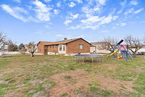 Rear view of house with a trampoline, brick siding, a playground, and a chimney