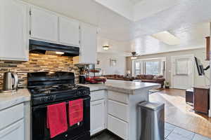 Kitchen with black range with gas stovetop, white cabinetry, a textured ceiling, a peninsula, and open floor plan