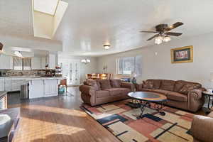 Living room with dark wood-style floors, a skylight, a textured ceiling, a chandelier, and a ceiling fan