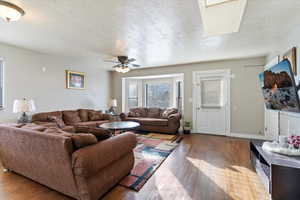 Living room featuring a textured ceiling, wood finished floors, and a ceiling fan