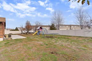 Fenced backyard featuring a trampoline, a playground, and a residential view