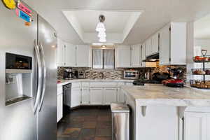Kitchen with appliances with stainless steel finishes, white cabinetry, a raised ceiling, a peninsula, and a kitchen bar