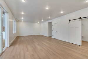 Unfurnished room featuring a barn door, light wood-type flooring, and recessed lighting