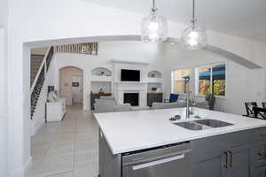 Kitchen featuring arched walkways, dishwasher, gray cabinetry, and light stone countertops
