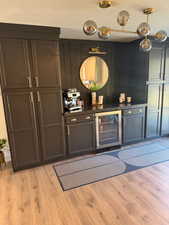 Bar featuring dark countertops, beverage cooler, and light wood finished floors