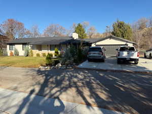 Single story home featuring concrete driveway, a front lawn, a chimney, and a garage