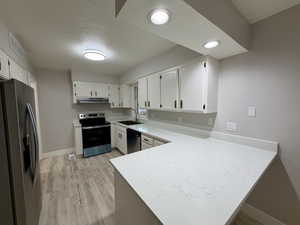 Kitchen with appliances with stainless steel finishes, a peninsula, white cabinets, light wood finished floors, and a textured ceiling