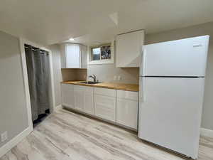 Kitchen with freestanding refrigerator, white cabinetry, butcher block counters, and light wood finished floors