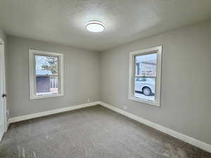 Carpeted empty room with a textured ceiling and baseboards