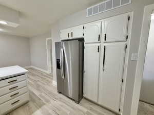 Kitchen with white cabinets, stainless steel fridge with ice dispenser, light wood-style floors, and light countertops