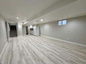 Below grade area featuring freestanding refrigerator, light wood-style flooring, stairway, and recessed lighting