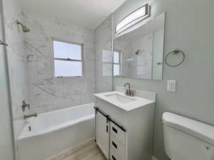 Bathroom with a combined bath / shower with marble appearance, a textured wall, vanity, plenty of natural light, and light wood finished floors