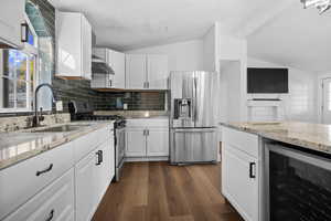 Kitchen featuring appliances with stainless steel finishes, light stone countertops, backsplash, wine cooler, and white cabinets
