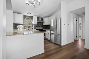 Kitchen featuring white cabinetry, tasteful backsplash, stainless steel appliances, light stone countertops, and a textured ceiling