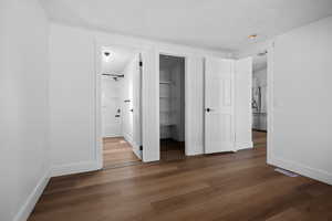 Unfurnished bedroom featuring dark wood-type flooring, a spacious closet, a textured ceiling, stainless steel fridge with ice dispenser, and connected bathroom