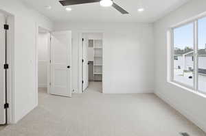 Unfurnished bedroom with a spacious closet, light carpet, ceiling fan, and recessed lighting
