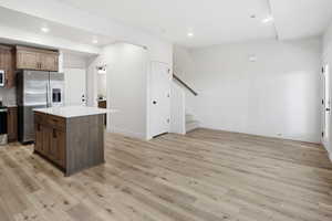 Kitchen featuring appliances with stainless steel finishes, light wood-type flooring, a center island, recessed lighting, and light stone counters