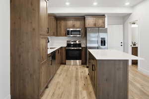 Kitchen with stainless steel appliances, light wood-style flooring, a center island, light stone counters, and recessed lighting
