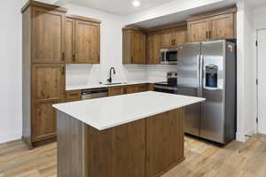 Kitchen with appliances with stainless steel finishes, a center island, light wood-style floors, and brown cabinetry