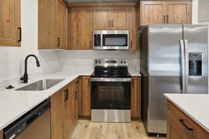 Kitchen with appliances with stainless steel finishes, brown cabinets, light stone counters, and light wood finished floors