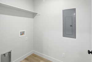 Laundry room featuring electric panel, light wood-type flooring, and washer hookup