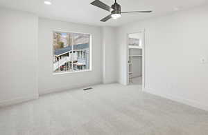 Unfurnished bedroom with a spacious closet, light colored carpet, and a ceiling fan