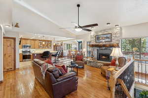 Living room with vaulted ceiling, plenty of natural light, light wood finished floors, ceiling fan, and a fireplace