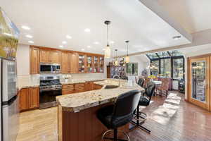 Kitchen with brown cabinets, tasteful backsplash, stainless steel appliances, glass insert cabinets, and recessed lighting