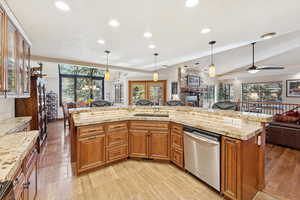 Kitchen with open floor plan, brown cabinets, stainless steel dishwasher, decorative light fixtures, and a center island with sink