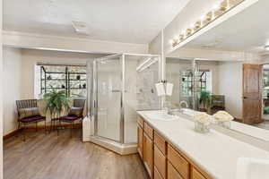 Full bath with a textured ceiling, light wood-type flooring, double vanity, and a stall shower