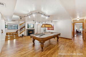 Rec room featuring a textured ceiling, a tiled fireplace, light wood finished floors, billiards, and track lighting