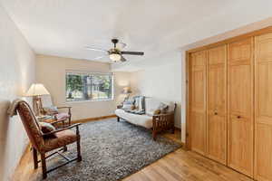 Sitting room with light wood-type flooring, ceiling fan, and a textured ceiling