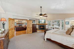Bedroom featuring a lit fireplace, light colored carpet, ceiling fan, a textured ceiling, and high vaulted ceiling
