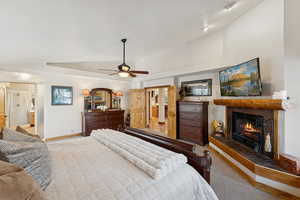 Carpeted bedroom with a fireplace, vaulted ceiling, connected bathroom, and ceiling fan